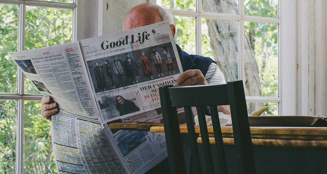Older man reads the newspaper in his kitchen
