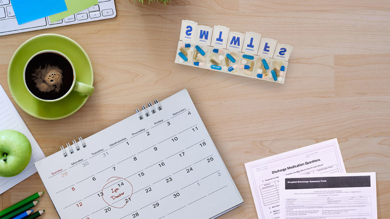Desk scene with coffee, pill box, calendar, and hospital discharge papers